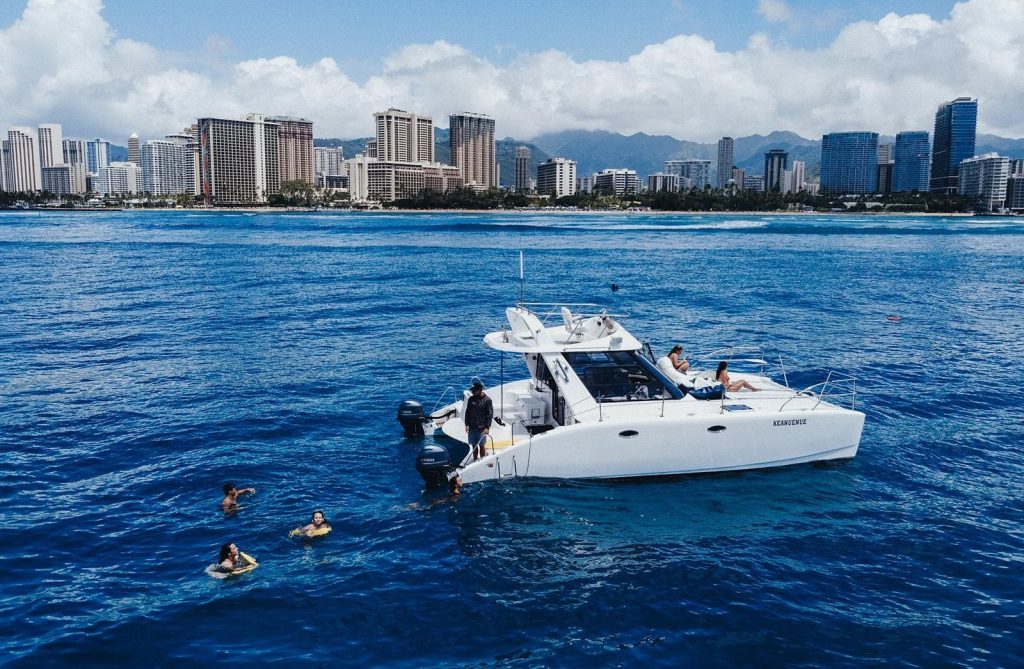 Catamaran near Honolulu skyline with swimmers enjoying Hawaii ocean outing.