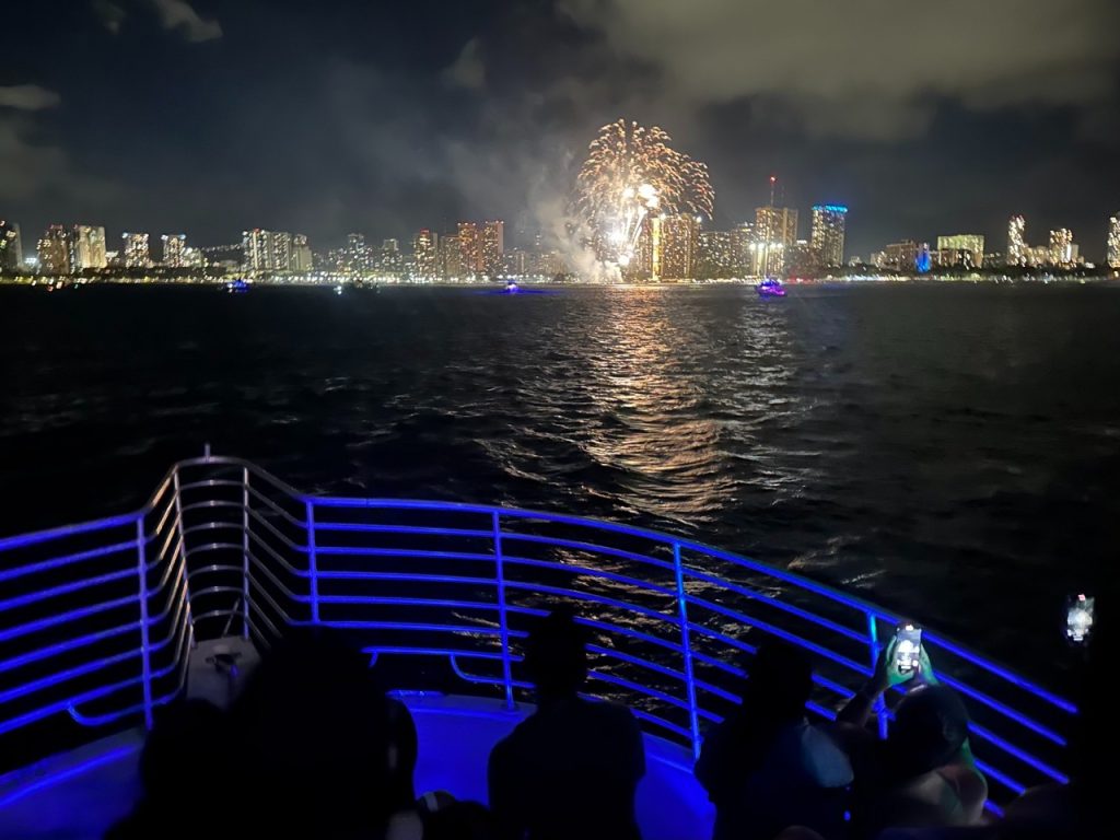 Waikiki fireworks cruise at night with bright fireworks reflecting on the ocean water.