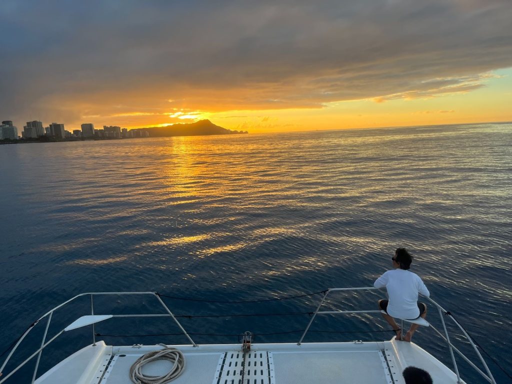 Waikiki sunset cruise with orange sky reflecting on calm ocean water.