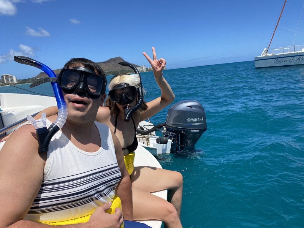 Couple wearing snorkel gear on a boat in turquoise Hawaiian waters.