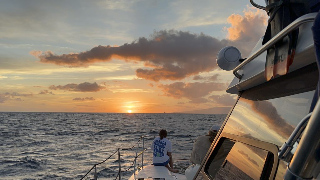Two people watching a golden ocean sunset from boat deck