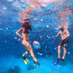 Snorkelers swimming underwater with bubbles and fish
