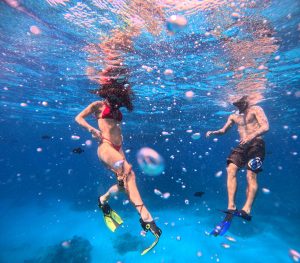 Snorkelers swimming underwater with bubbles and fish