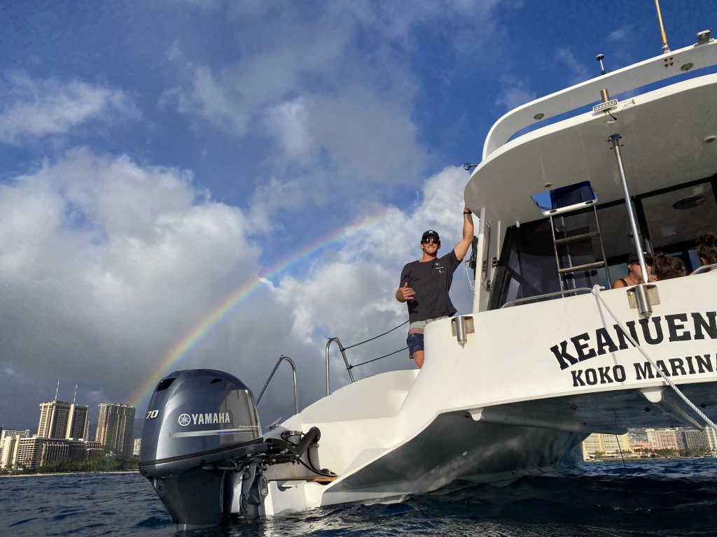 Crew member on Keanuenue boat with rainbow in background