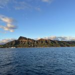 Scenic view of Diamond Head in Oahu from the ocean, with blue water and a partly cloudy sky.