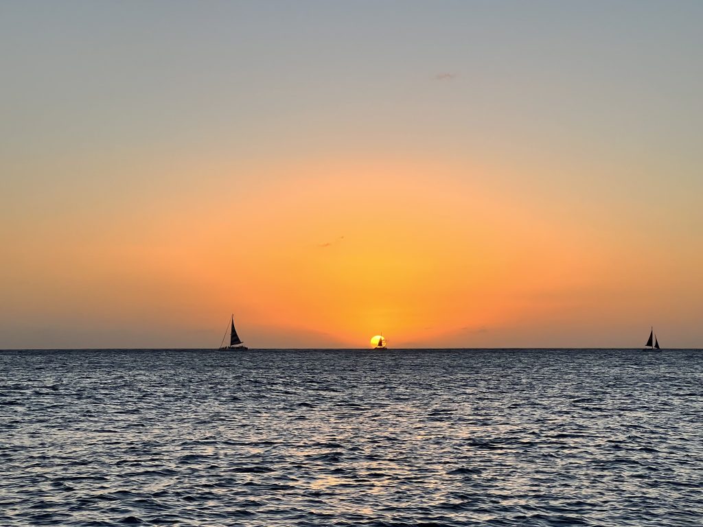 Sunset over the ocean with silhouetted sailboats